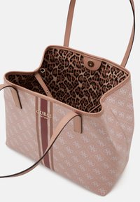 Vaaleanpunainen käsilaukku, jossa on leopardikuosiset sisävuoret, logo-design, kaksi pitkää kahvaa ja kultaiset yksityiskohdat.