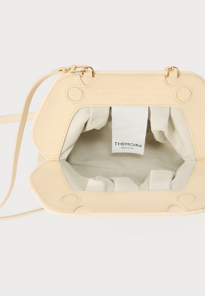 Μπεζ δερμάτινη τσάντα χειρός με ανοιχτό πάνω μέρος, εσωτερικό από κρεμ ύφασμα, χρυσά εξαρτήματα και ετικέτα που γράφει "THEMOIRè Made in Italy" στο εσωτερικό.