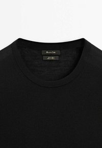 Pull noir à col rond avec des étiquettes de marque et de matériau visibles à l'intérieur du col.