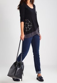 Svart långärmad topp med V-ringning, med ett mönstrat nederdel och detaljer i strass. Matchad med mörka jeans och en svart handväska.