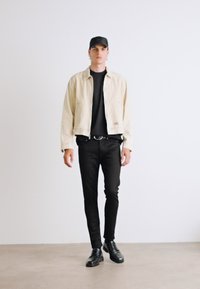 Chaqueta de mezclilla beige, camisa negra ajustada, pantalones negros slim, zapatos negros y gorra negra. Textura suave, diseño sencillo.