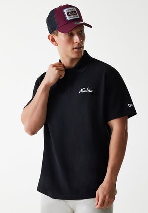 Black polo shirt with short sleeves and a collar; features white "New Era" embroidery on the chest. A maroon trucker cap is worn.