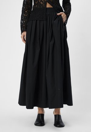 Sorte, plisserede midi-nederdel med høj talje og sidelommer, lavet af et glat stof. Bæres med sorte slip-on sko.