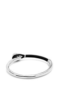 Pulsera de metal plateado curvada, parcialmente conectada por un cordón de cuero negro con un pequeño detalle de cuenta de plata en el cordón.