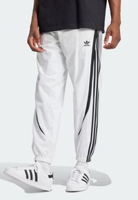 Vita träningsbyxor med svarta sidostrekar, elastiska muddar och en Adidas-logotyp på låret. Kombineras med vita sneakers med svarta detaljer.