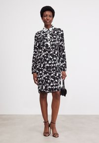 Long-sleeve dress in black and white featuring an animal print design. Collared neckline, knee-length, with a straight cut and soft fabric.