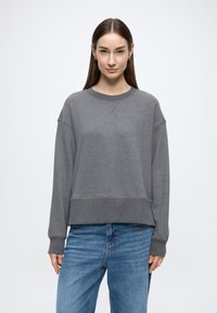 Γκρι φούτερ με στρογγυλή λαιμόκοψη, χαμηλωμένους ώμους, ριμπ μανσέτες και τελείωμα, σε συνδυασμό με ανοιχτό μπλε τζιν. Ομαλή υφή υφάσματος.