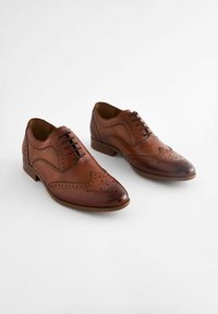 Chaussures habillées en cuir marron présentant un design classique à brogue, un bout pointu, des perforations détaillées et un petit talon empilé.