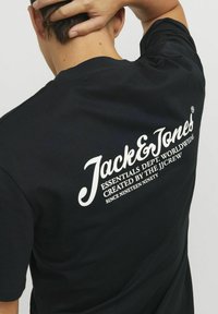 Camiseta de algodón negra con texto blanco en la parte posterior: "Jack & Jones ESSENTIALS DEPT. WORLDWIDE CREADO POR EL EQUIPO JJ DESDE MIL NOVECIENTOS NOVENTA."