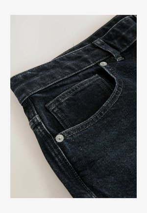 Jean en denim foncé avec une légère texture, comprenant une poche arrière et un détail de bouton en métal près de la taille, ainsi qu'une couture contrastante.