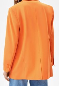 Blazer arancione con maniche lunghe, revers a punta e polsini con due bottoni. Il tessuto è liscio e il design presenta una vestibilità su misura con spacco posteriore.