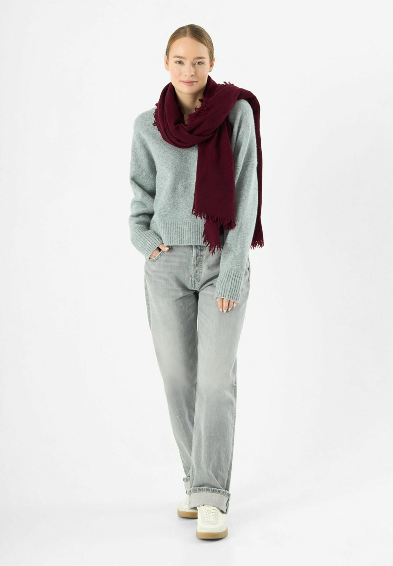 Maglione grigio chiaro a maglia con orlo a coste; abbinato a jeans grigio chiaro a vita alta e una sciarpa bordeaux scuro con bordi sfilacciati.
