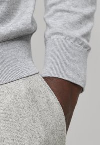 Tessuto grigio di un maglione con polsini a coste, abbinato a pantaloni grigi chiari e testurizzati. Un primo piano rivela le cuciture e i dettagli di design casual.