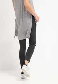 Grå, lång tunika med sidofickor, ihop med slim-fit svarta jeans och vita sneakers med svarta detaljer och mönster.