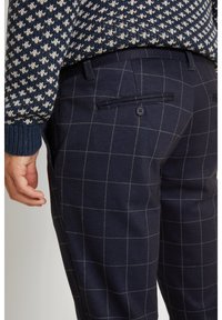 Navy blue plaid trousers made of a textured fabric, featuring a slim fit, two back pockets, and button closures with gray lines.