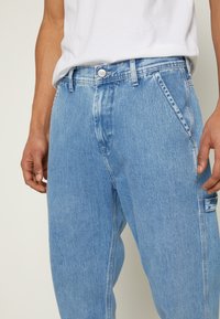 Ljusblå denimjeans med avslappnad passform, som har en knappstängning, framfickor och en blekt struktur längs låren.