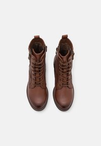 Botas de tobillo de cuero marrón con cordones frontales, cremalleras laterales y forro de piel cálido, vistas desde arriba sobre un fondo blanco.