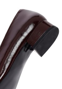 Bordeaux gepatineerde leren pump met een slank ontwerp, vierkante neus en een lage, gestructureerde zwarte hak. Reflecterend oppervlakdetail.