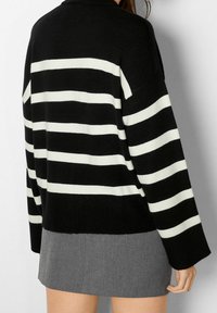 Pull en maille rayé noir et blanc, doté d'une coupe ample, de manches larges et d'un col côtelé, associé à une jupe grise.