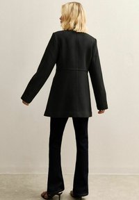 Zwarte wolmixjas met lange mouwen, een aansluitende pasvorm en een licht uitlopende onderkant. Glad oppervlak en schone stikseldetails.