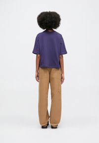 Camicia corta viola con collo rotondo abbinata a pantaloni cargo beige larghi con grandi tasche laterali.