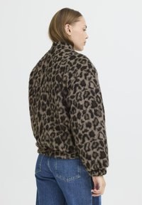 Veste imprimée léopard en tissu doux et texturé. Elle a une coupe décontractée, avec un col montant et des manches larges, associée à un jean bleu.