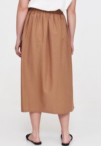 Brąska, średniej długości spódnica z elastycznym paskiem w talii, wykonana z lekkiego materiału. Gładka tekstura z prostym krojem, sięgająca nad kostki.