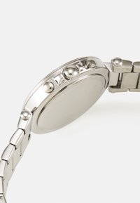 Montre-bracelet en métal argenté avec un boîtier rond, une couronne proéminente, des détails texturés et un design de bracelet à maillons. Surface lisse et réfléchissante.