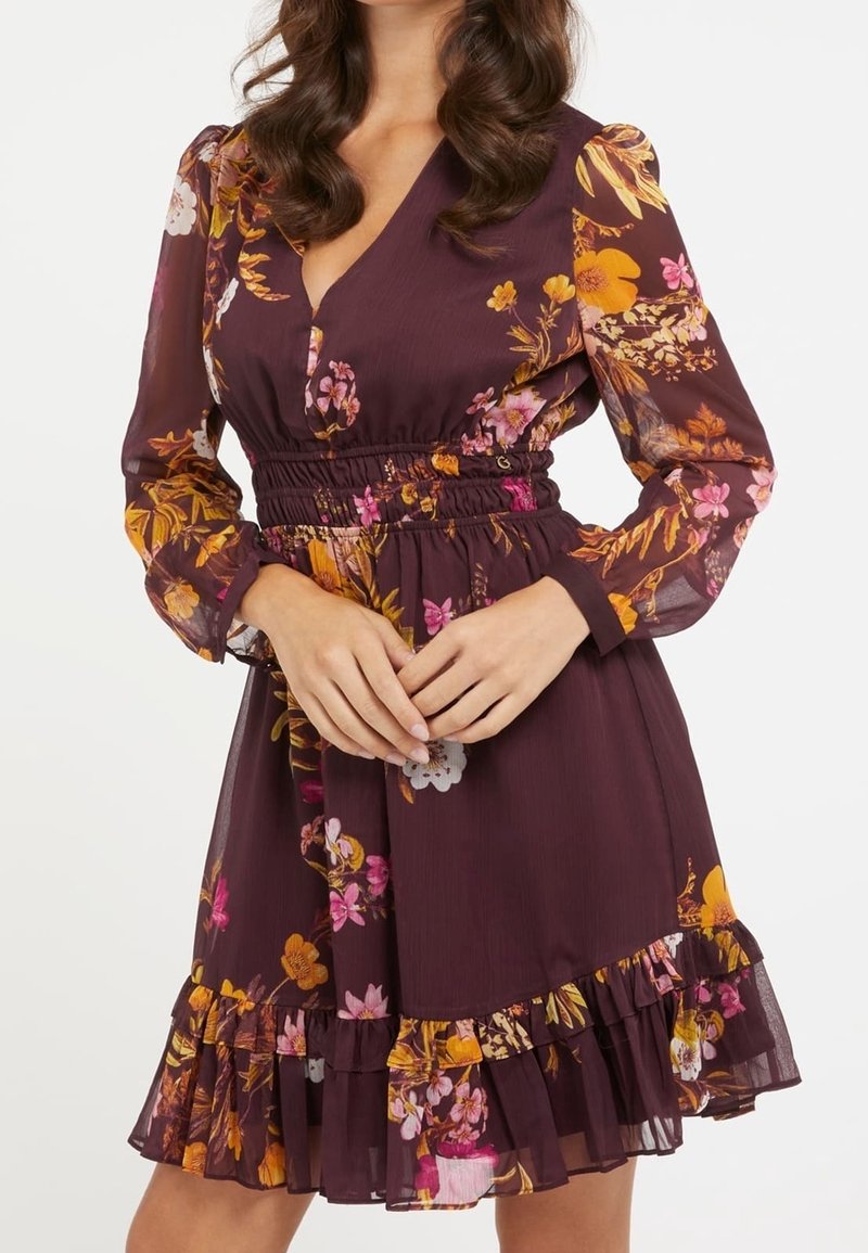 Robe fleurie avec un décolleté en V profond, des manches longues en voile, une taille élastique et un ourlet à volants. Présente des motifs floraux vibrants jaunes, roses et blancs sur un fond sombre.