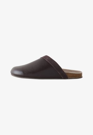 Dunkelbraune Leder-Slipper mit Wildlederbesatz und Kork-Fußbett, von der Seite vor weißem Hintergrund gezeigt.