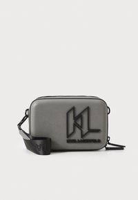 Borsa a tracolla rettangolare grigia con una texture liscia, caratterizzata da un logo nero in rilievo e una tracolla regolabile. Chiusura a zip superiore.