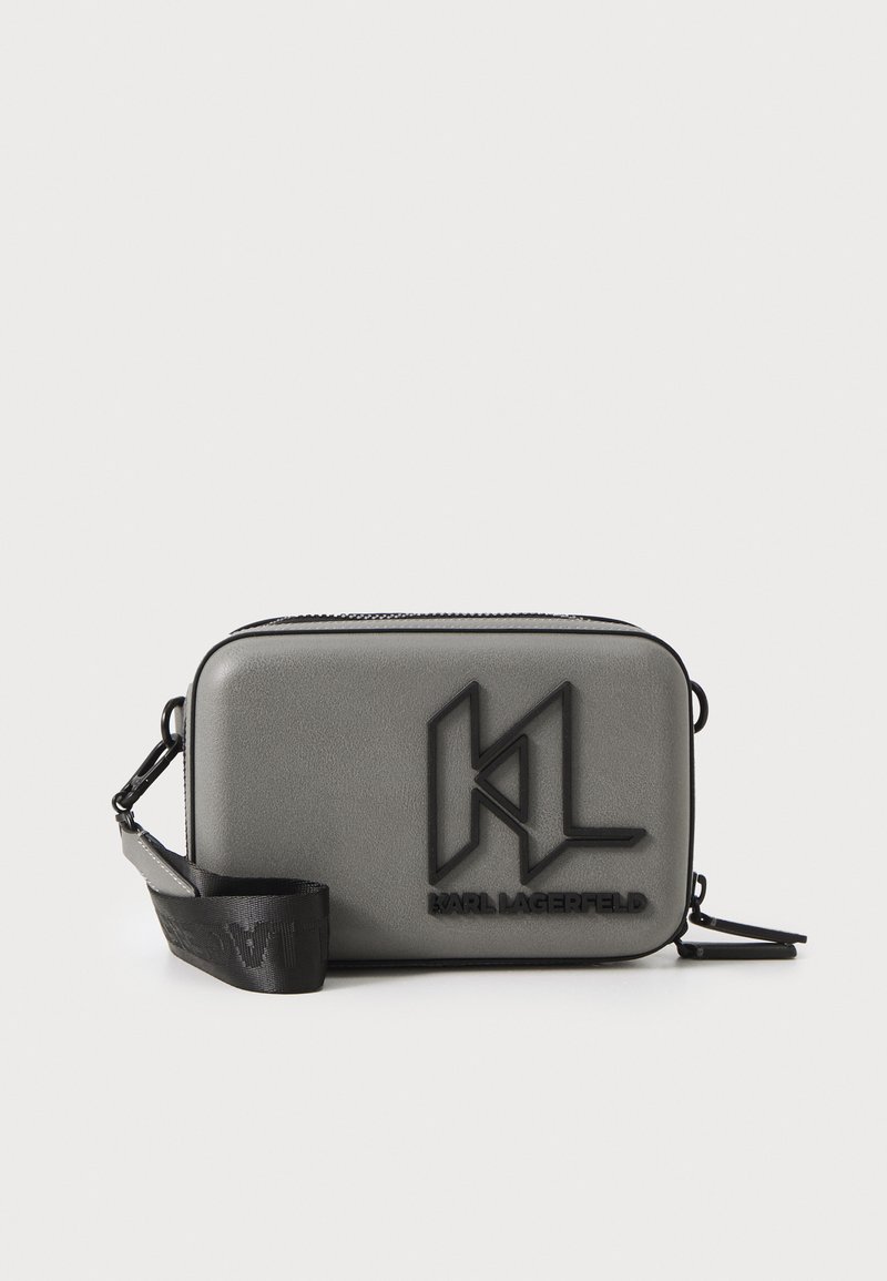 Borsa a tracolla rettangolare grigia con una texture liscia, caratterizzata da un logo nero in rilievo e una tracolla regolabile. Chiusura a zip superiore.
