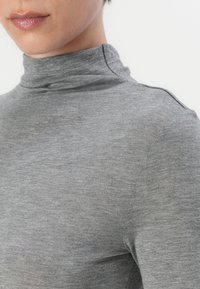 Grå højhalset sweater lavet af blødt stof, med en høj krave og glat struktur, pyntet med subtile syninger på skulderen.