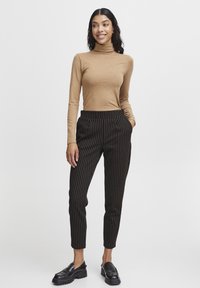 Maglione a maniche lunghe con collo a imbuto abbinato a pantaloni neri a righe sottili con accenti arancioni e tasche laterali, completato da mocassini neri chunky.
