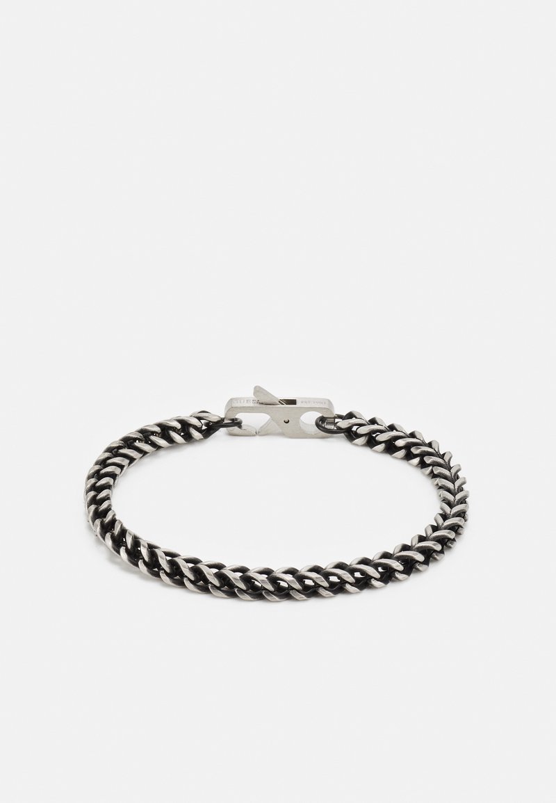 Bracelet chaîne épaisse à maillons curb en ton argent avec fermoir rectangulaire posé sur un fond gris clair.