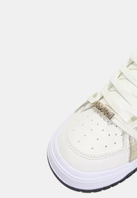 Sneaker in pelle bianca con punta perforata e dettagli dorati. Presenta lacci color crema e un accento argentato texturizzato sul lato.