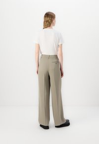 Pantaloni evazați, de culoare khaki, confecționați dintr-un material ușor, având un buzunar la spate și un talie înaltă. Asortați cu un simplu tricou alb.