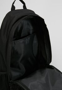 Zaino nero con un'esterno in tessuto testurizzato. L'interno presenta una fodera nera liscia e una tasca a parete. Chiusura con zip e spallacci regolabili.