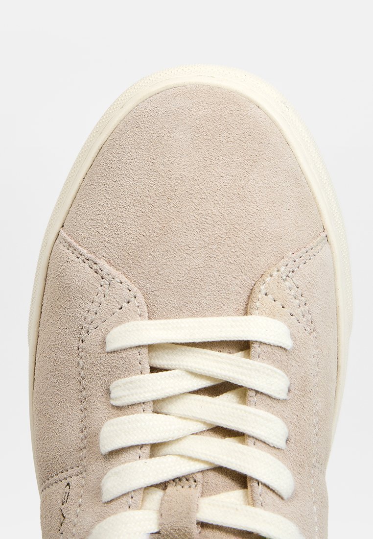Beige mockasin-sneakers med krämfärgade snören, rund tå, platt gummisula och minimalistiska sömnadsdetaljer, designade för avslappnad användning.