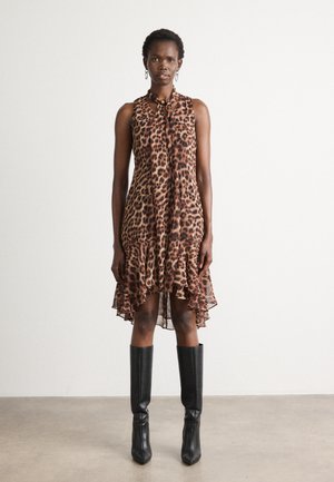 Robe sans manches à imprimé léopard avec un col à nouer, un ourlet superposé et une texture transparente, assortie à des bottes noires à talons aiguilles hauteur genou.