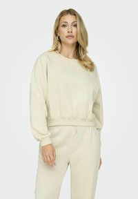 Felpa color crema con orlo e polsini a costine, caratterizzata da una vestibilità ampia e una consistenza morbida, abbinata a pantaloni abbinati con vestibilità rilassata.