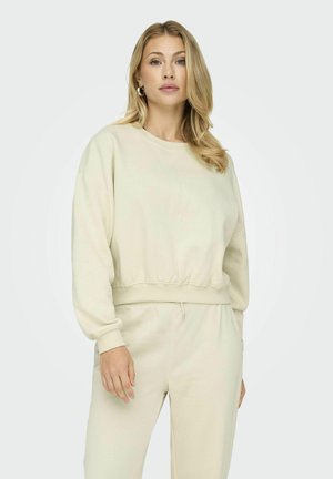 Felpa color crema con orlo e polsini a costine, caratterizzata da una vestibilità ampia e una consistenza morbida, abbinata a pantaloni abbinati con vestibilità rilassata.