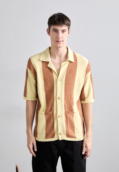 Chemise en tricot texturé avec des rayures jaunes et marron alternées, fermeture à boutons, manches courtes et deux poches avant.