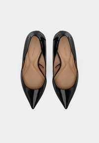 Une paire de ballerines noires en cuir verni à bout pointu avec des semelles intérieures rembourrées beiges, vues de dessus sur un fond blanc.