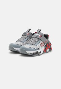 Sivobiele tenisky Skechers s pixelovým vzorom, červenou a čiernou kockovanou podrážkou, sivými šnúrkami a suchým zipsom na zapínanie.