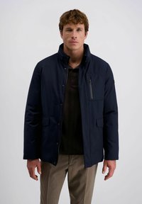 Navyblauwe jas met een rechtopstaande kraag, vooraan ritssluiting en drukknoopsluiting, twee voorzakken en een gehalveerde borstzak. Vlotte stoftextuur.