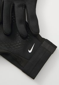Czarne sportowe rękawice wykonane z teksturowanej tkaniny, dopasowane do kształtu dłoni, z białym logo Nike na mankiecie.