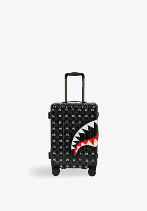 Maleta rígida negra con diseño de boca de tiburón, pequeños iconos blancos repetidos y un asa telescópica extendida sobre cuatro ruedas.