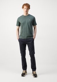 T-shirt en coton vert à manches courtes, associé à un chino marine foncé et des baskets noires avec des accents beiges et une semelle texturée.