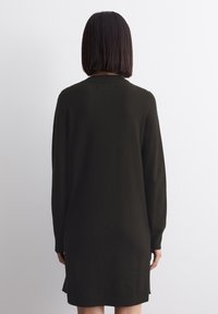 Robe à manches longues de couleur vert foncé en tissu doux, avec une coupe décontractée et un col rond, dotée d'un ourlet légèrement plus long à l'arrière.